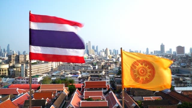 Thai national flag and Dharma Chakra flag fluttering above cityscape