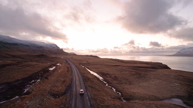 Car driving along a coastal road at sunset