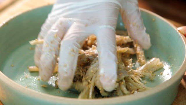 Close-up of a hand in gloves mixing seasoned vegetables in a bowl.