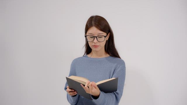 Long haired woman wearing glasses reading a book in a quiet room