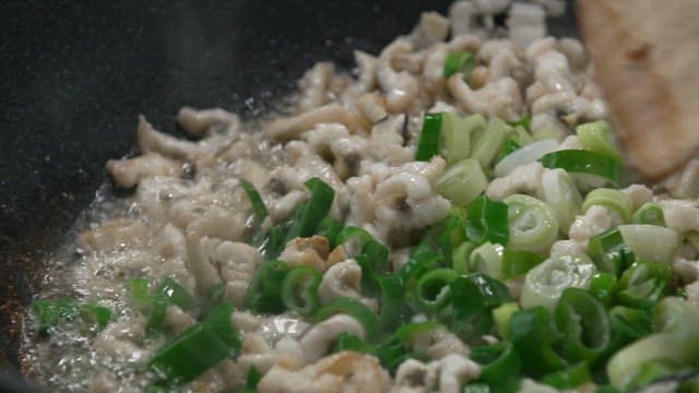 Cooking seafood in a frying pan with trimmed eel and green onions