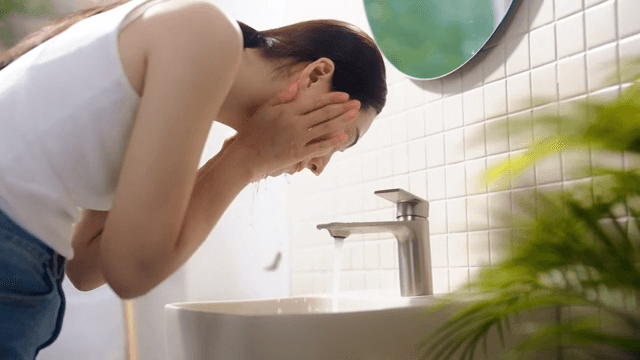 Woman washing face at bright bathroom sink