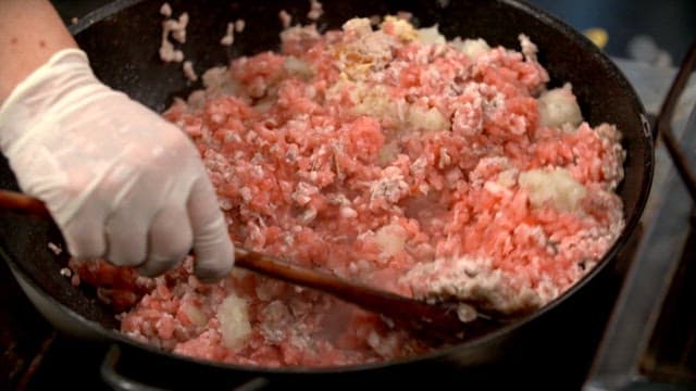 Ground meat being cooked in a pan with a wooden spatula