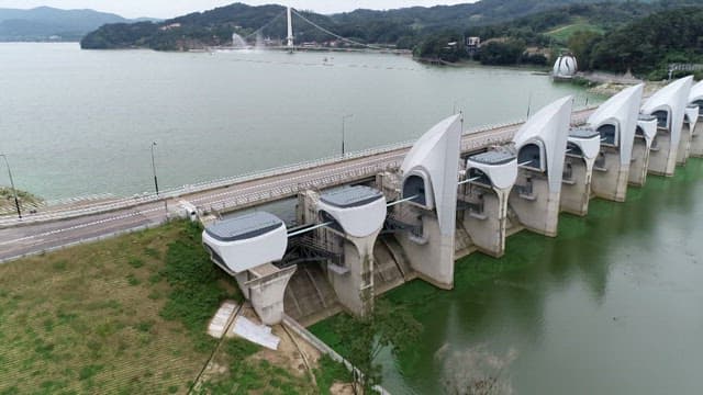 Aerial view of a dam with lush green hills and a river