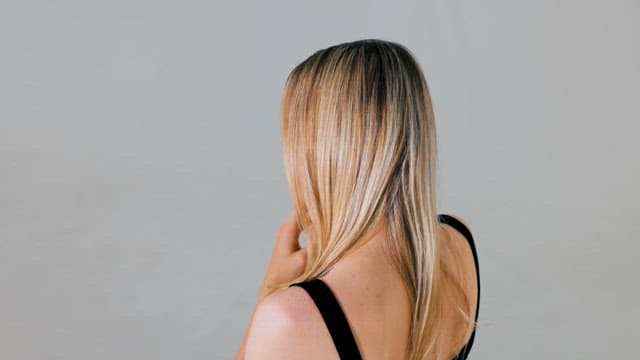 Back of a Blonde Woman Looking at a White Wall