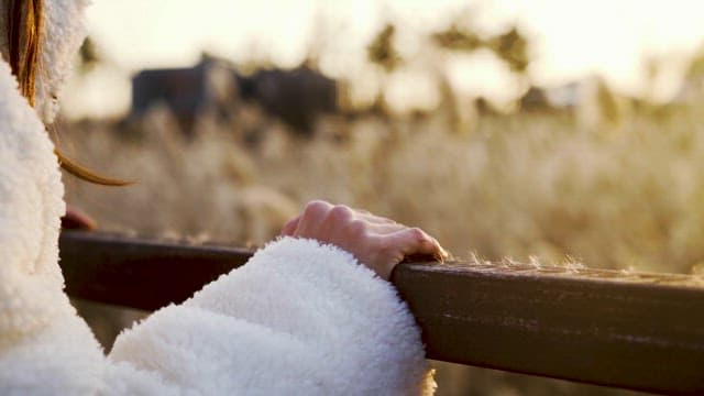 Person enjoying leisurely time leaning against a wooden railing on an autumn afternoon