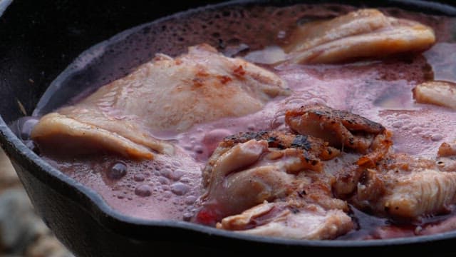 Chicken in frying pan with tomato sauce and spices being added