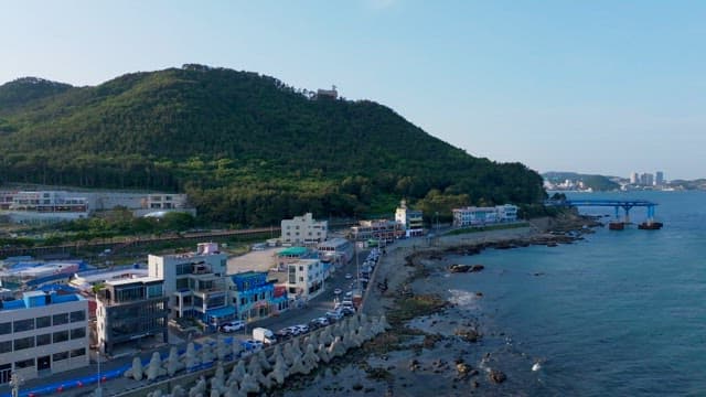 Coastal road with buildings and green hill in background