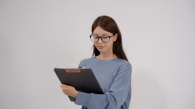 Long haired woman wearing glasses writing something on clipboard