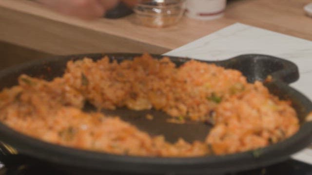 Cooking kimchi fried rice with egg in a hot pan on a stove with wooden spatula