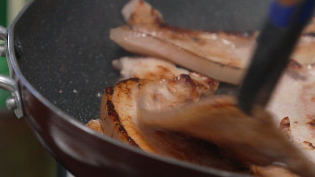 Cutting the grilled pork belly in a frying pan into bite-size pieces with scissors