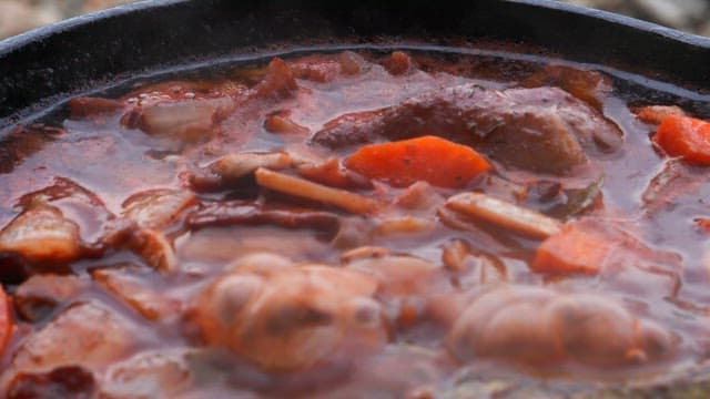 Simmering stew full of vegetables and meat in a black pot