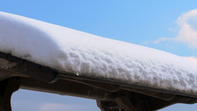 Snow-covered roof of a wooden structure under a bright blue sky