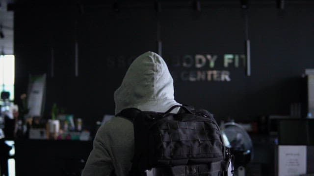 Person entering a dimly lit fitness center with a backpack