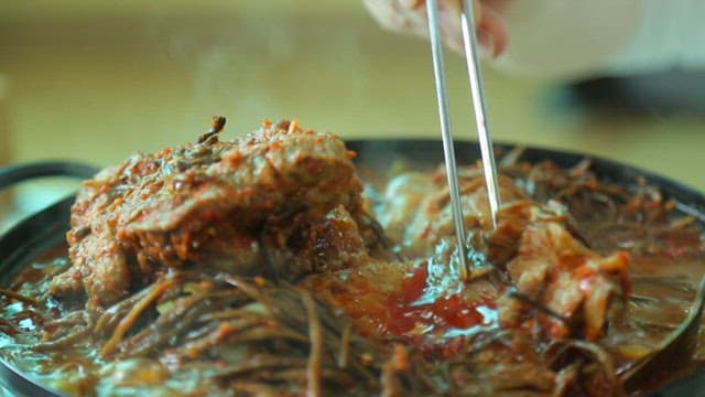 Plate of pork backbone stew meat with sweet potato stem salad picked with chopsticks