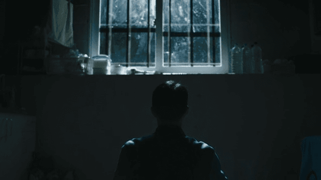 Man sitting under a barred window in prison