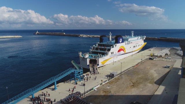 Ferry docked at a sunlit seaport with passengers