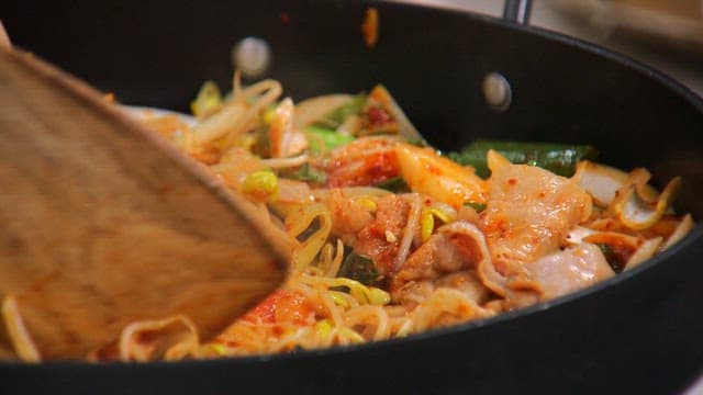 Bean sprout bulgogi cooked on a hot plate with a wooden spatula