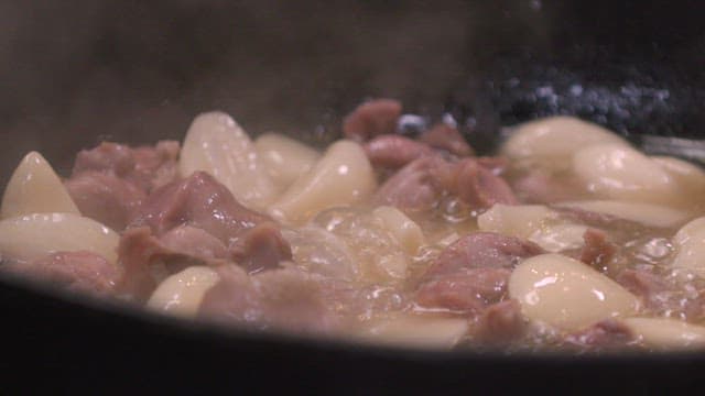 Meat and garlic are sizzling in a pan with oil