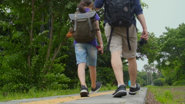 Father and daughter walking along a path in a lush park