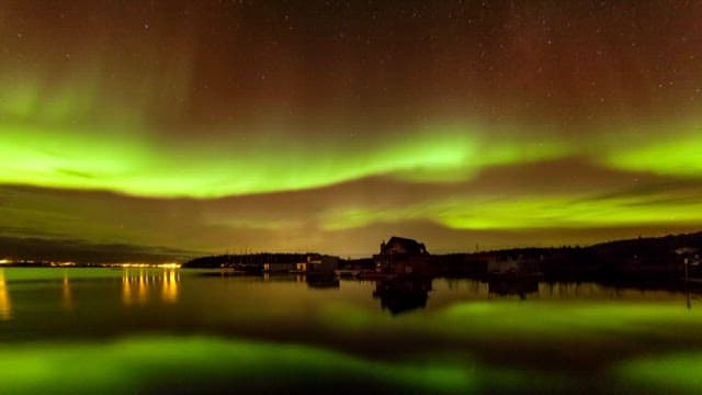 Aurora glowing in the sky above a quiet lake town