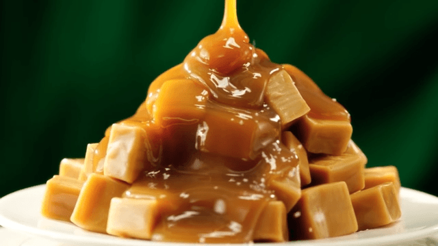 Pouring caramel sauce over caramels piled on a white plate