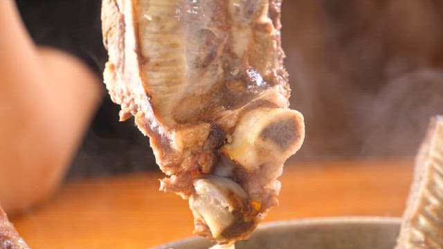 Taking out ribs from a steaming hot Galbitang with tongs