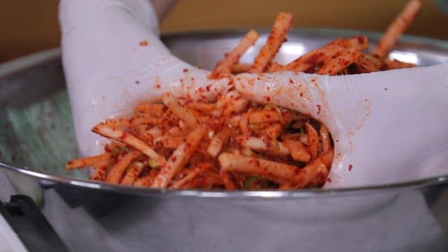 Mixing julienne Korean radish salad in a metal bowl