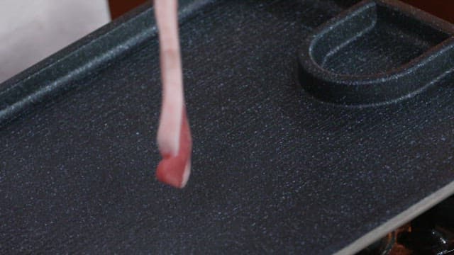 Raw pork belly being placed on a grill