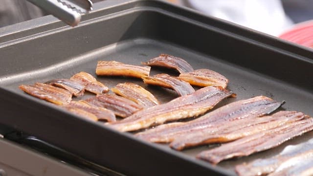 Grilling half-dried saury on a pan with tongs