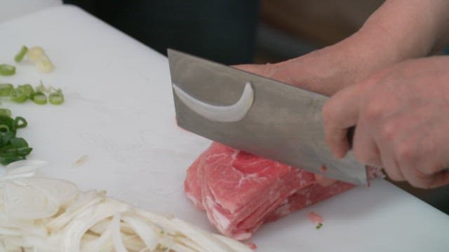 Slicing fresh meat with vegetables on a cutting board