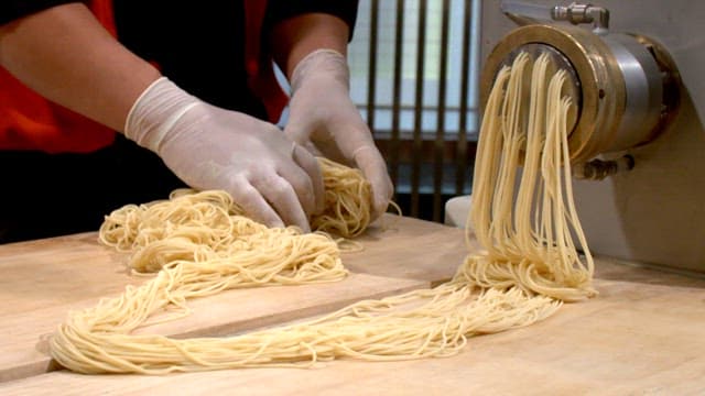 Chef handling pasta being extruded from a machine