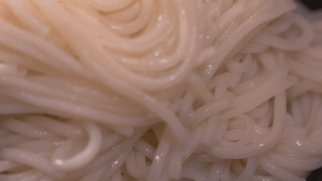 Hands preparing boiled noodles in a bowl