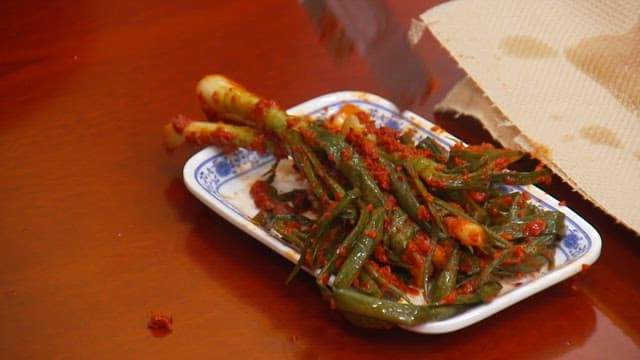 Chopsticks holding green onion kimchi on a plate on a wooden table