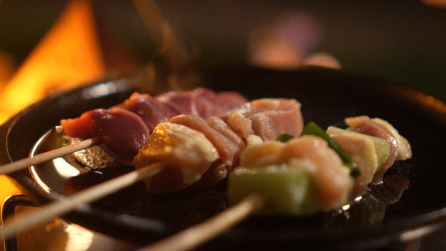 Skewered meat cooking on a pan over a gas burner at night