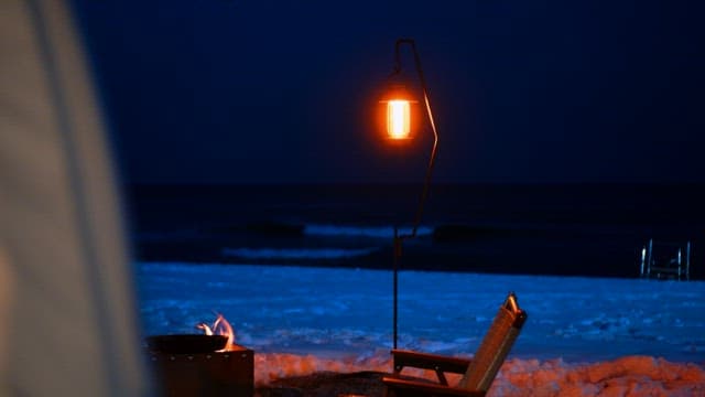 Snowy beach at night with a lit lantern and fire pit