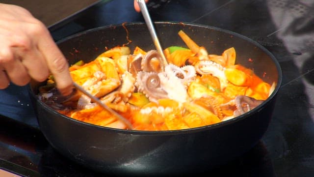 Cooking spicy webfoot octopus tteokbokki with a frying pan and spoon