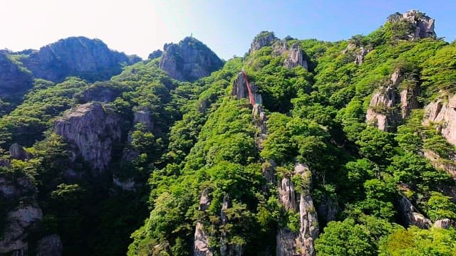 Tree-covered rocky mountain with a red suspension bridge visible