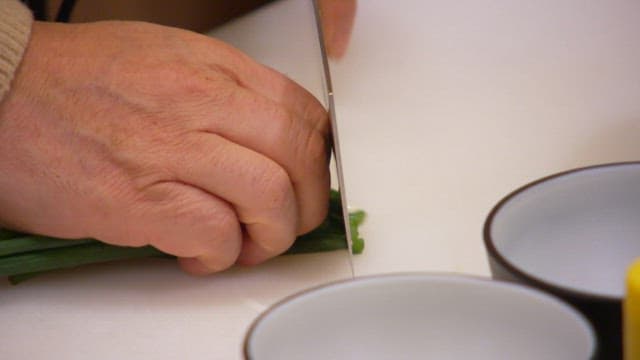 Person chopping green onions that will rise to the top on a cutting board