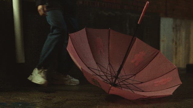 Person passing by an overturned umbrella on a rainy night