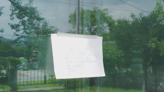 Paper with poem written on window reflecting green trees 