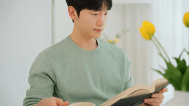 Man reading a book and drinking coffee in a bright room