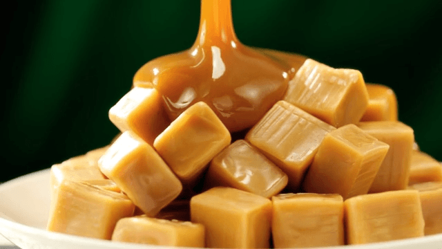 Pouring caramel sauce over caramels piled on a white plate