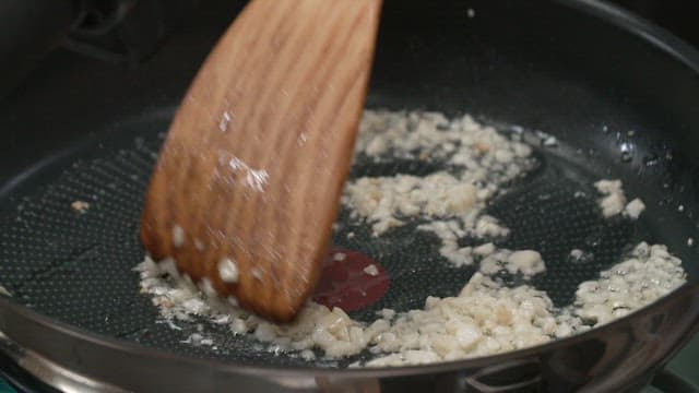 Frying chopped garlic in oil in a pan with a wooden spatula