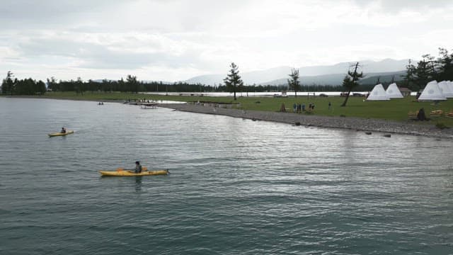 People kayaking on a serene lake with distant mountains