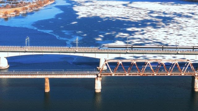 Train Crossing Bridges Over Snow-Covered  River