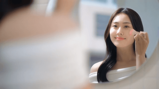 Woman applying makeup with a brush in front of a mirror