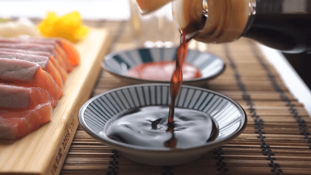 Pouring soy sauce into a bowl near sliced salmon
