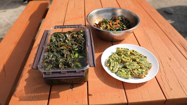 Spinach pickles, salad, and rolled omelet on a wooden table