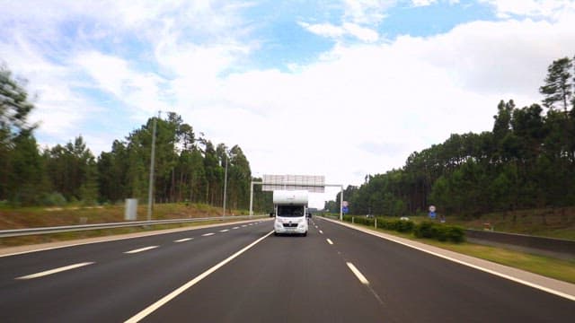 White Recreational Vehicle Driving on a Forest-lined Highway